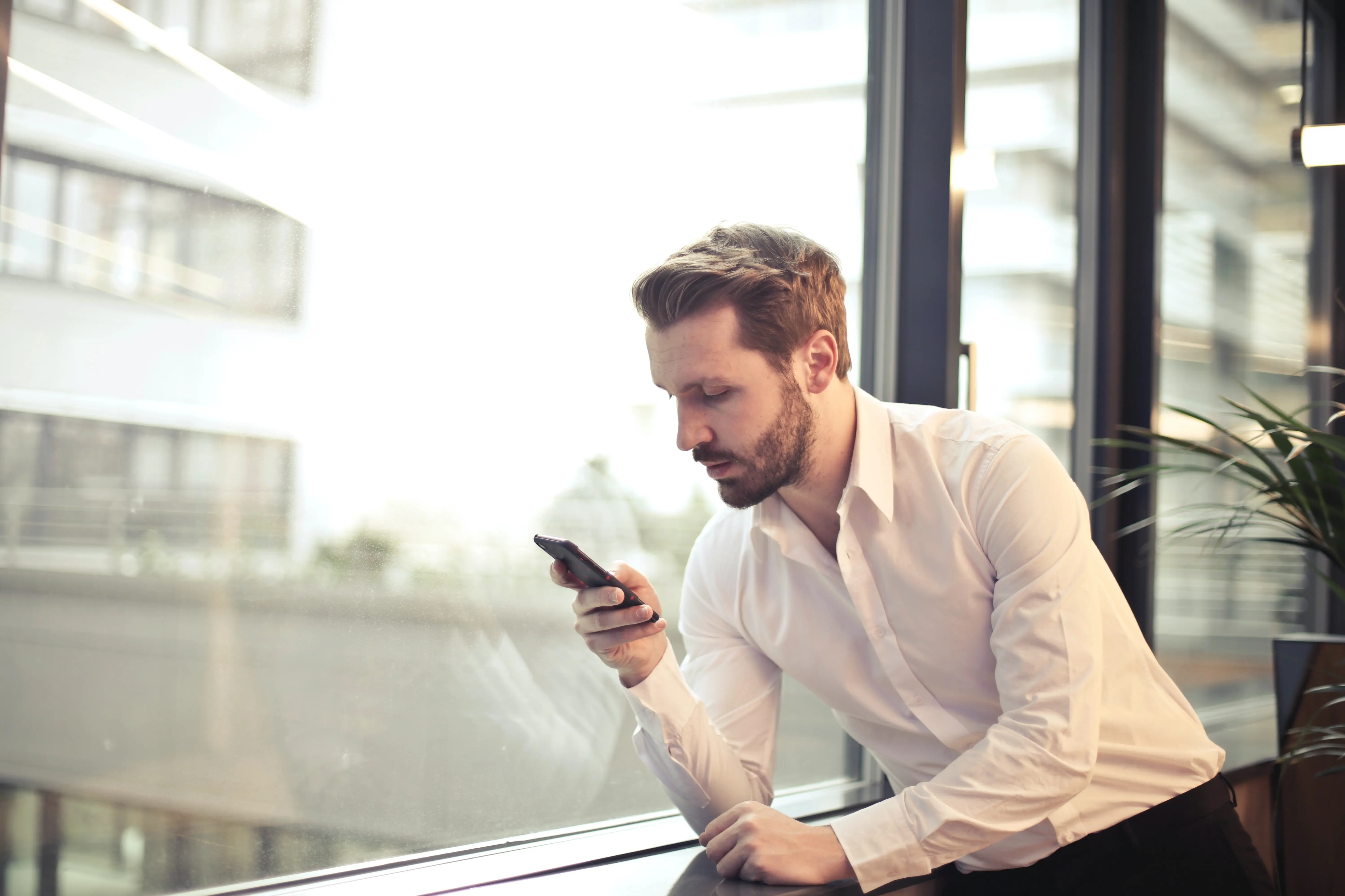 Man in white shirt looking at phone in front of window